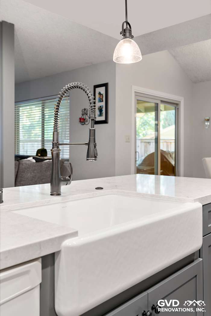 White farmhouse sink with a modern pull-down faucet, gray cabinetry, and pendant lighting in a remodeled kitchen