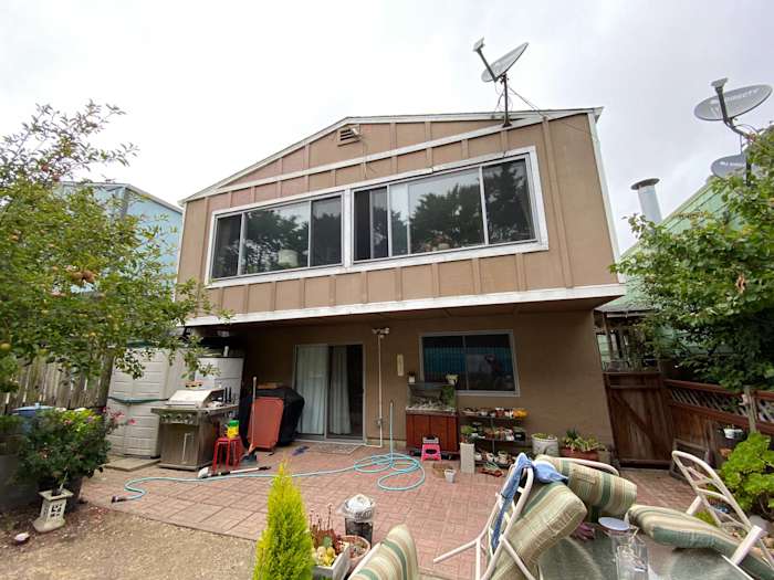 Daly City home exterior featuring old siding and patio area with outdoor furniture and greenery