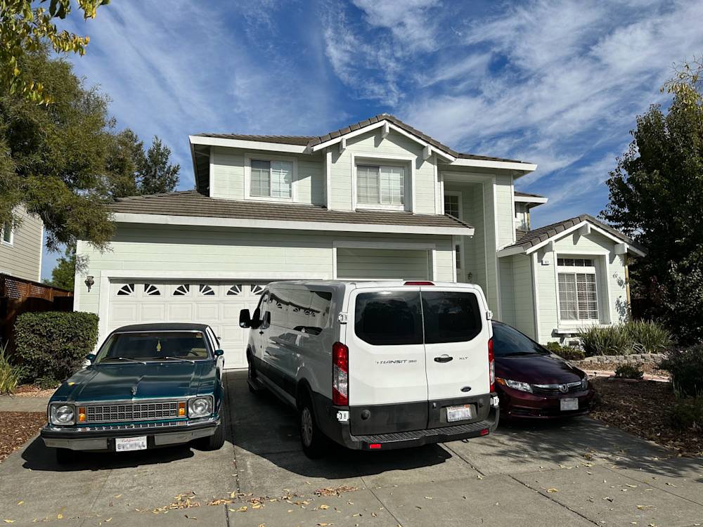 Two parked cars and a white van in front of a two-story Sacramento home with a grey roof and landscaped yard