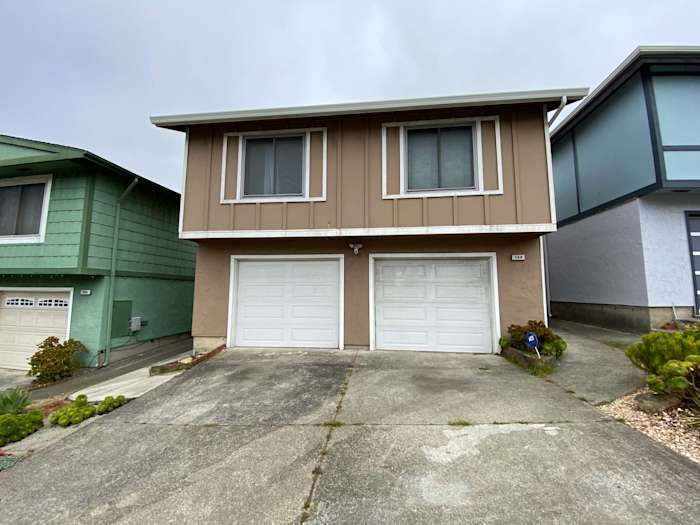 Brown home exterior with old siding, two-car garage, and gray driveway in Daly City