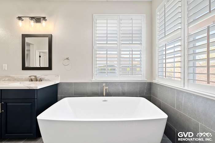Modern master bathroom featuring a freestanding tub, dark cabinetry, and light gray tile flooring