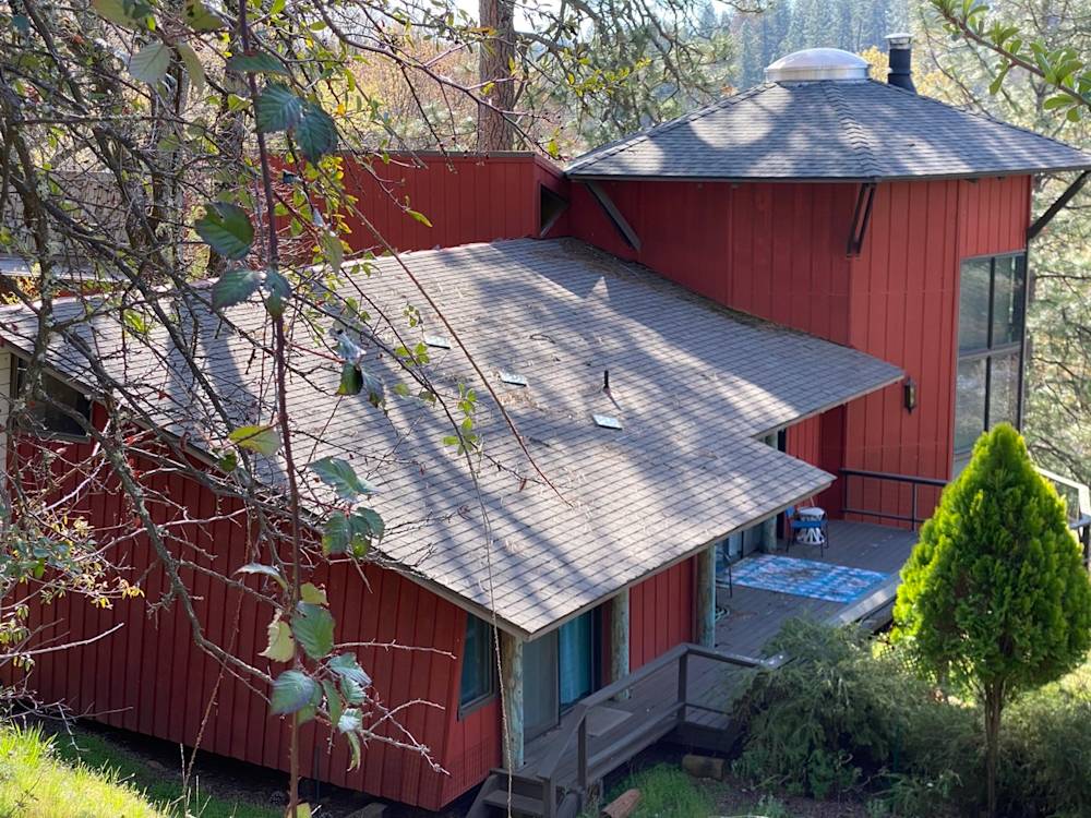 Red exterior home in Northern California, surrounded by trees and landscaping, featuring a large deck