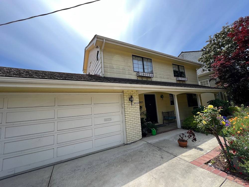 Two-story yellow house with a concrete driveway and colorful garden, located in Sacramento