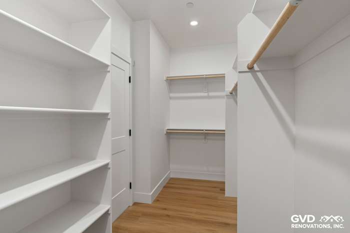 Bright walk-in closet featuring white shelving, wooden hanging rods, and light oak flooring