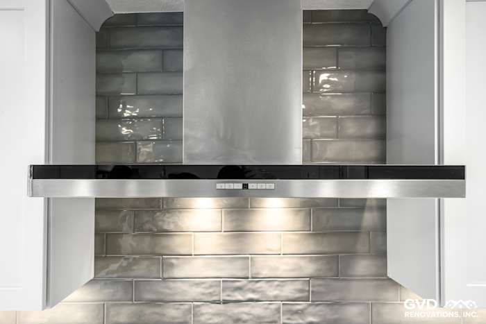 Modern kitchen range hood with stainless steel finish over sleek gray subway tile backsplash