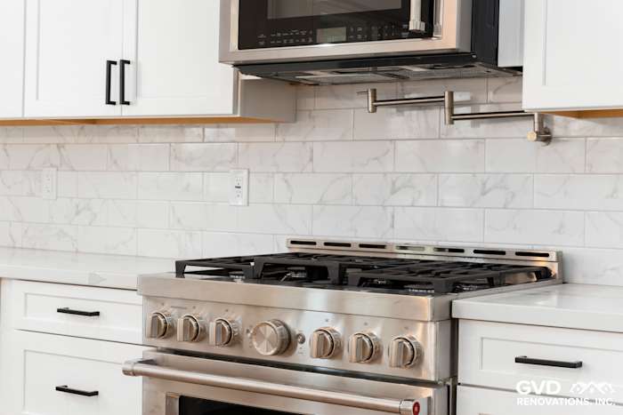 Stainless steel gas range with marble backsplash and white cabinetry in a custom kitchen in Paradise, CA