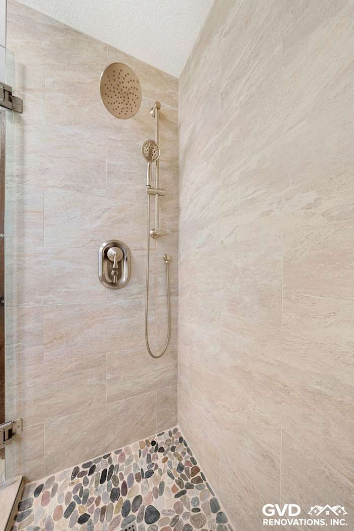 Modern shower with pebble flooring, rain showerhead, and sleek fixtures in a renovated bathroom