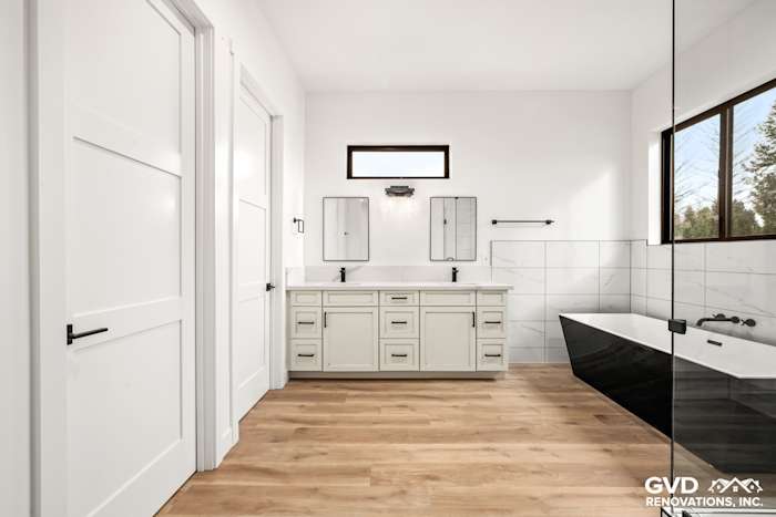 Modern bathroom in Paradise with sleek black bathtub, dual vanities, white cabinetry, and natural wood flooring
