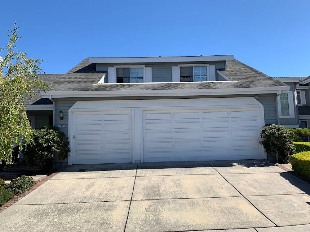 Gray two-car garage with white doors surrounded by green shrubs in Sacramento