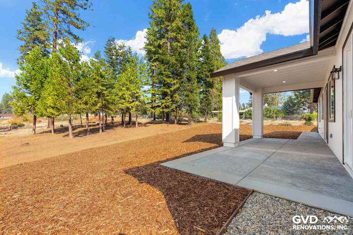 New construction home exterior in Paradise, CA featuring a spacious patio and landscaped yard with trees