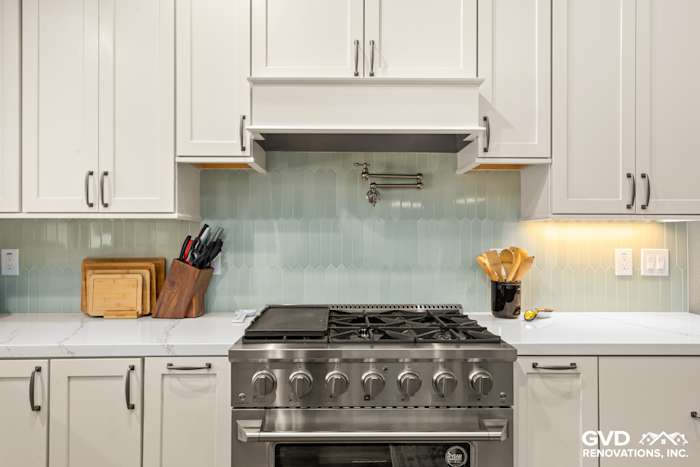 Modern kitchen featuring a stainless steel range, light green backsplash, and white custom cabinets in Carmichael
