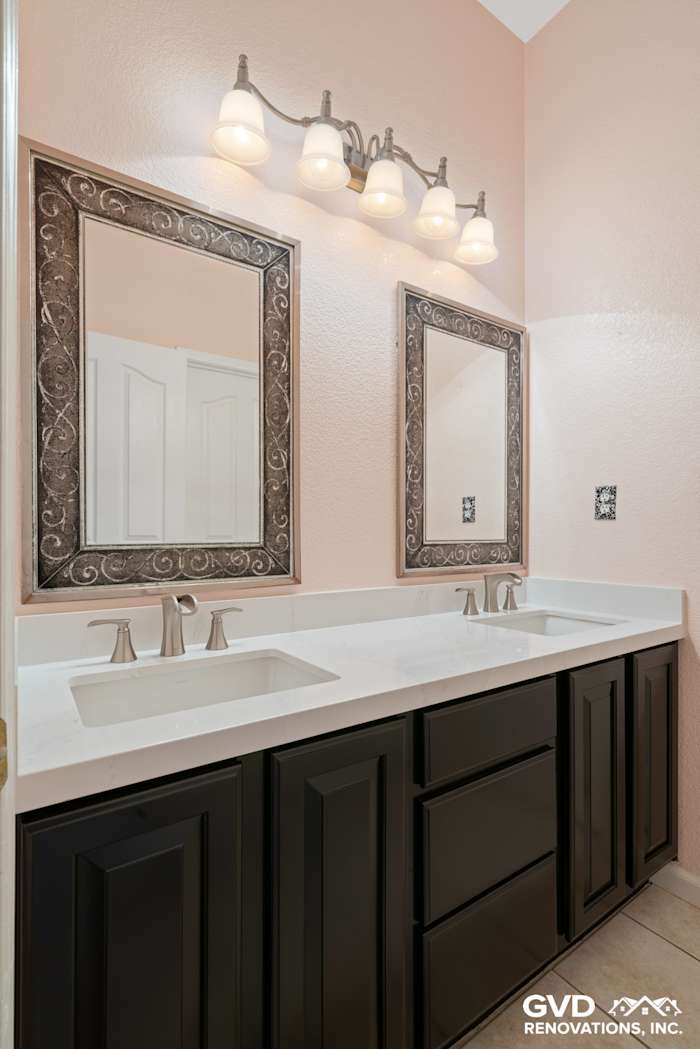 Modern bathroom vanity with black cabinetry, dual sinks, and elegant mirrors against soft pink walls