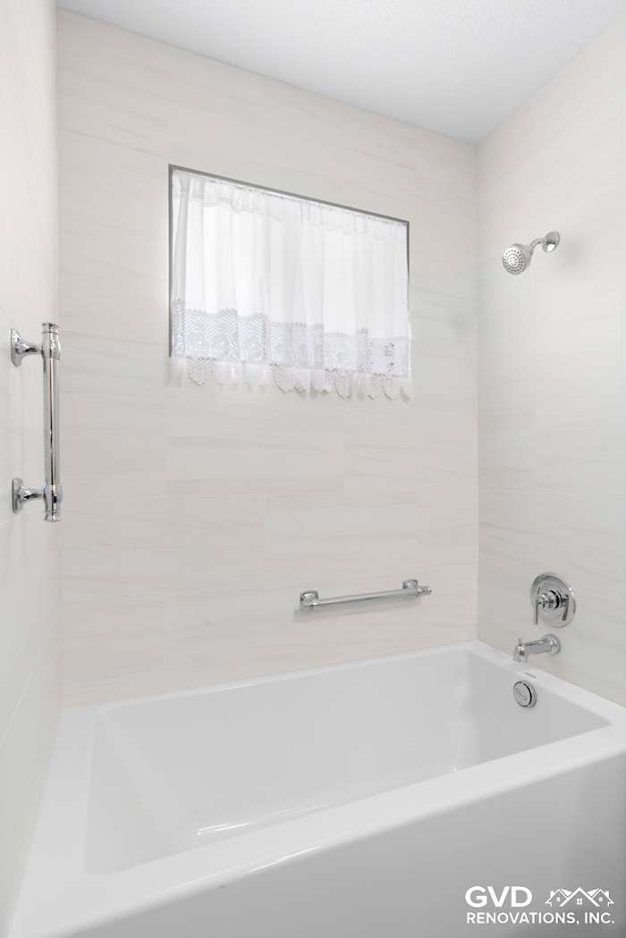 Modern bathtub with a sleek design, chrome fixtures, and a decorative window curtain in a renovated bathroom