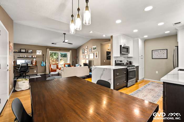 Bright kitchen with wood dining table, white cabinets, stainless steel appliances, and modern pendant lighting