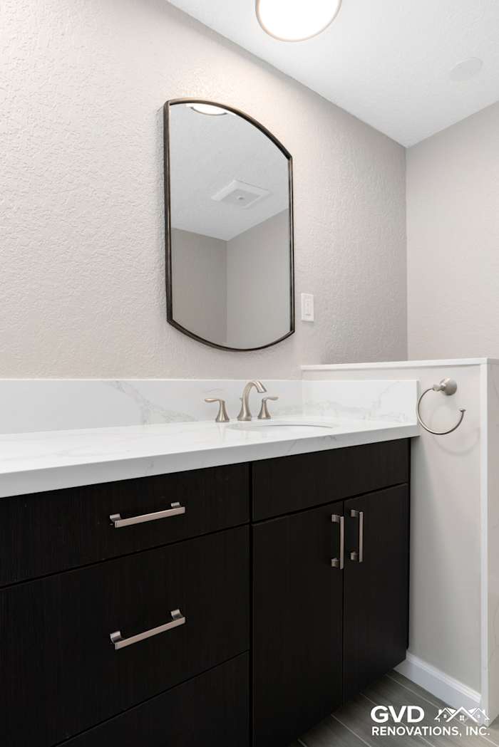 Modern bathroom vanity with dark cabinetry, marble countertop, and round mirror in Rocklin remodel
