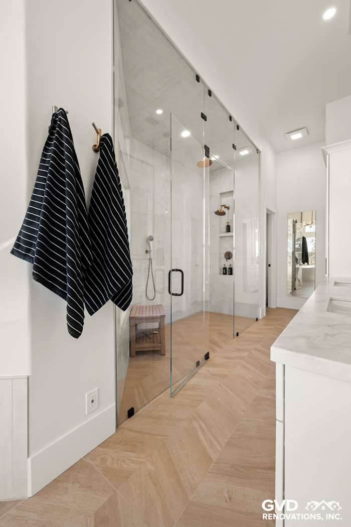 Luxurious master bathroom with glass steam shower, heated herringbone tile floor, and stylish hanging towels