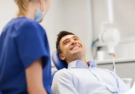 A man in his thirties is lying in the dentist chair while a female dentist explains to him the difference between temporary and permanent dentures. 