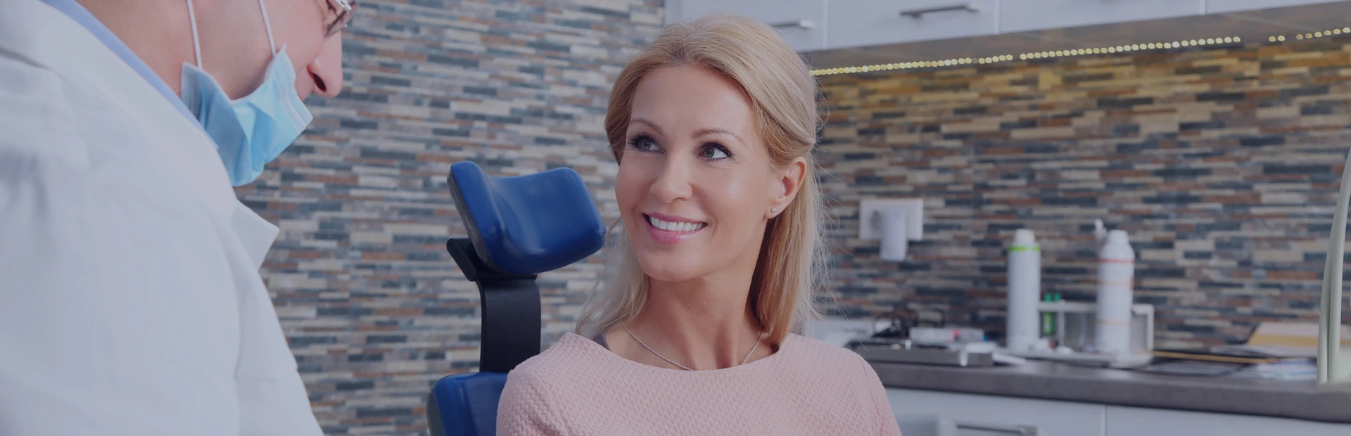 A woman is sitting in the dentist chair with her dentist explaining to her the reasons and solutions for ill fitting dentures. 