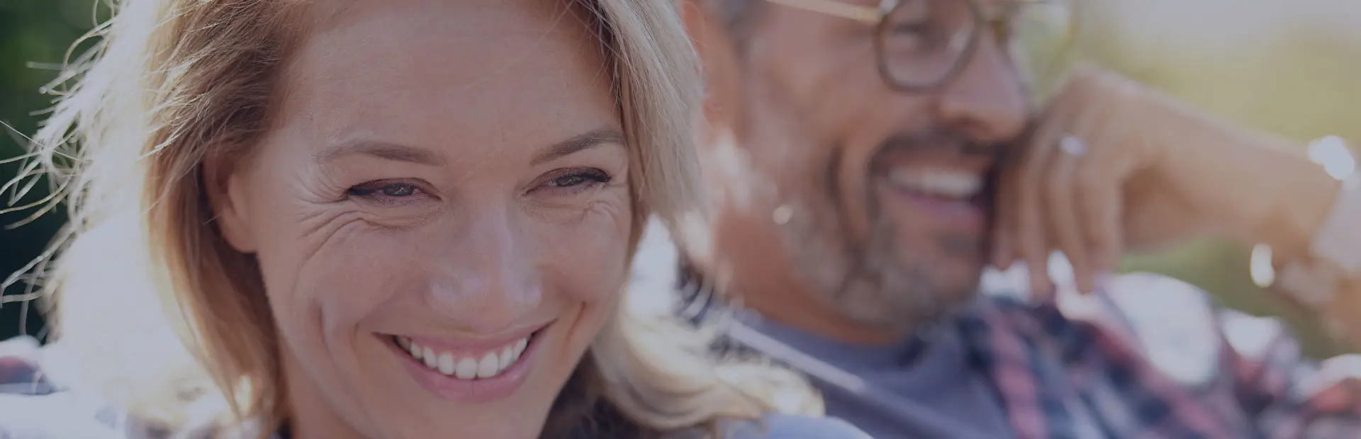 A couple are outdoors smiling in the sun, as they are getting used to wearing new dentures