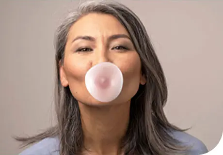 A woman is seen blowing bubble gum, showing you can chew gum with dentures. 