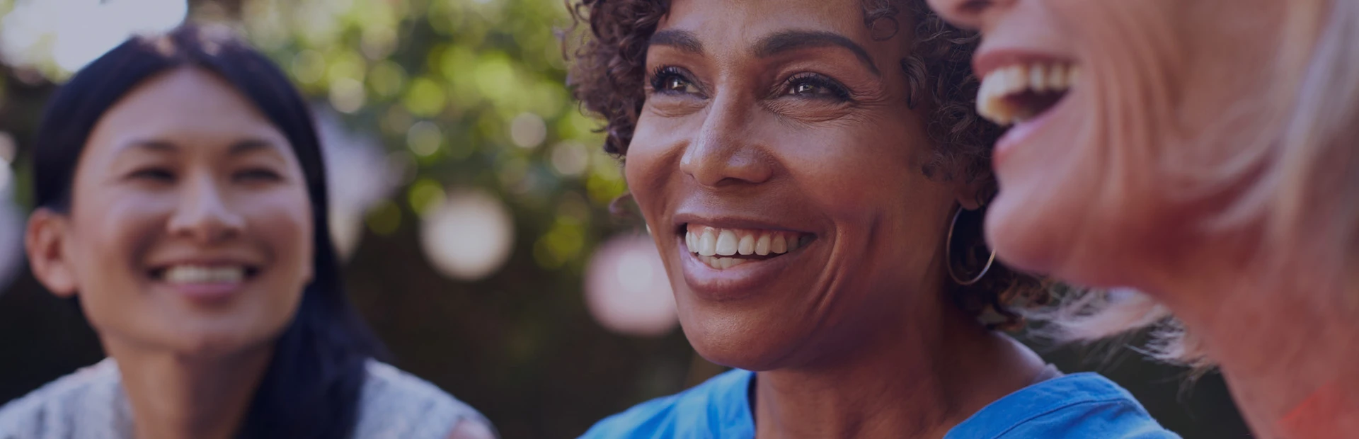 A group of female friends in their early 50s and 60s are sitting in a park smiling and discussing how much dental implants cost.