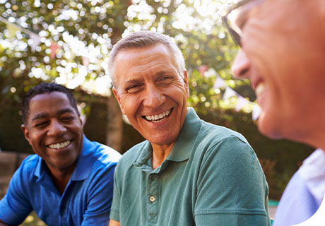 A group of male friends in their fifties are smiling in a garden, as they discuss getting used to full or partial dentures.