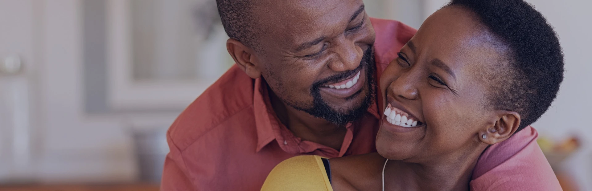 A couple in their 40s are hugging and smiling, the woman is wearing dentures, but is happy and confident as she has learned everything she needs to know about denture adhesive thanks to Fixodent. 