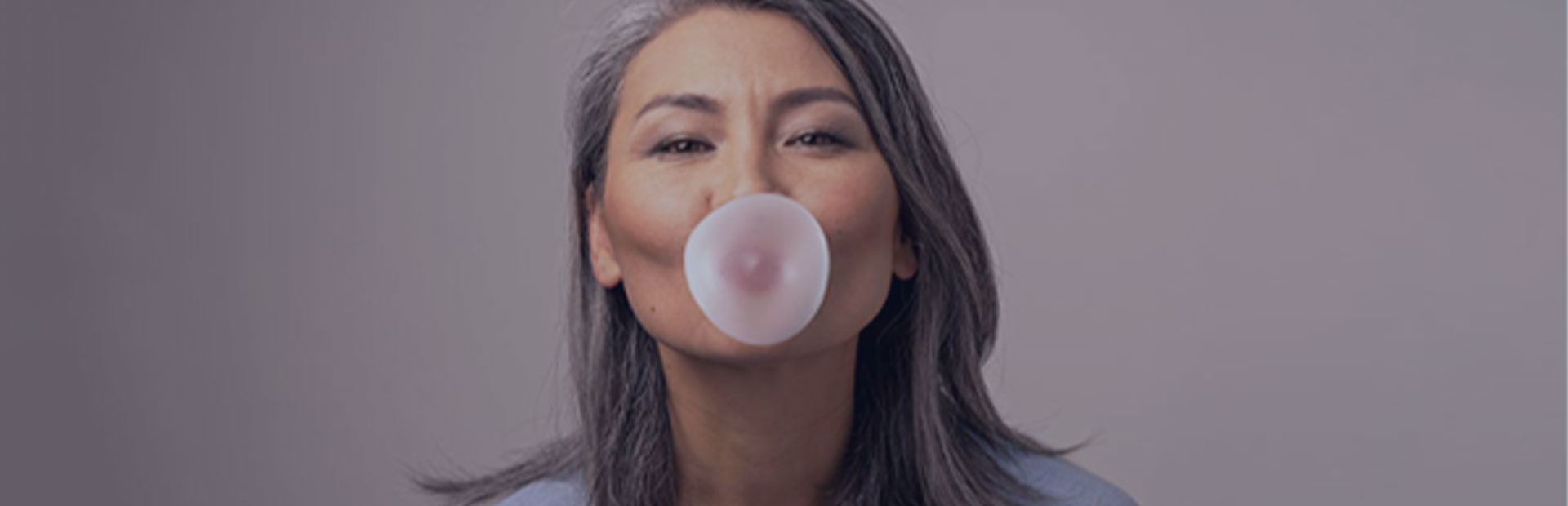 A woman in her 50s blows some bubble gum, as she knows she can still chew gum with dentures while using Fixodent. 