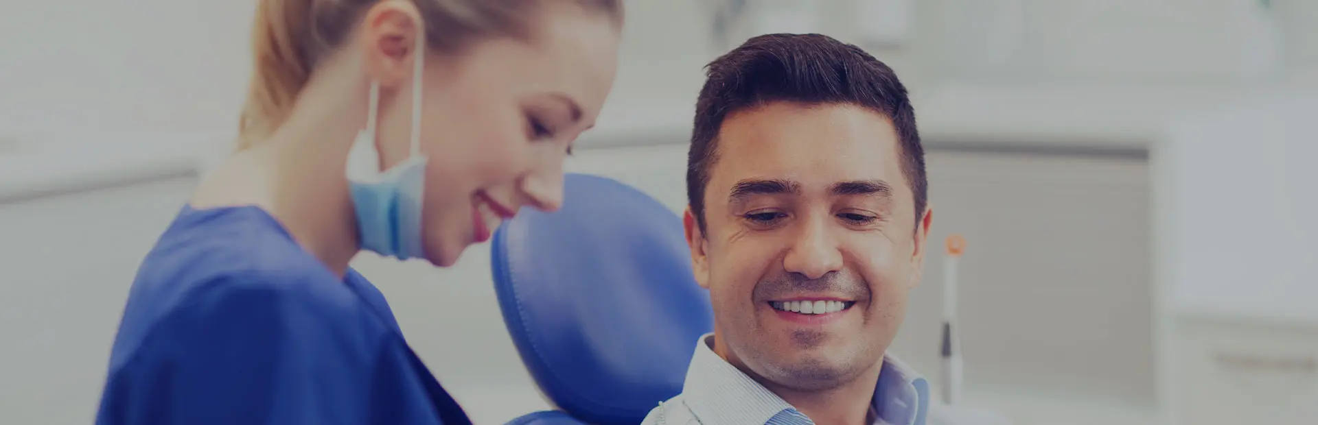 A dentist holds a tablet in her hand showing the screen to her patient, while she answers his frequently asked questions about denture adhesive. 