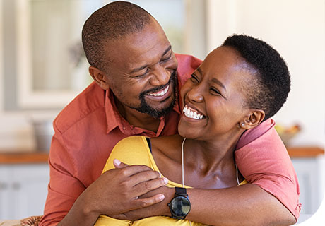 A couple in their 40s are hugging and smiling, the woman is wearing dentures, but is happy and confident as she has learned everything she needs to know about denture adhesive thanks to Fixodent. 