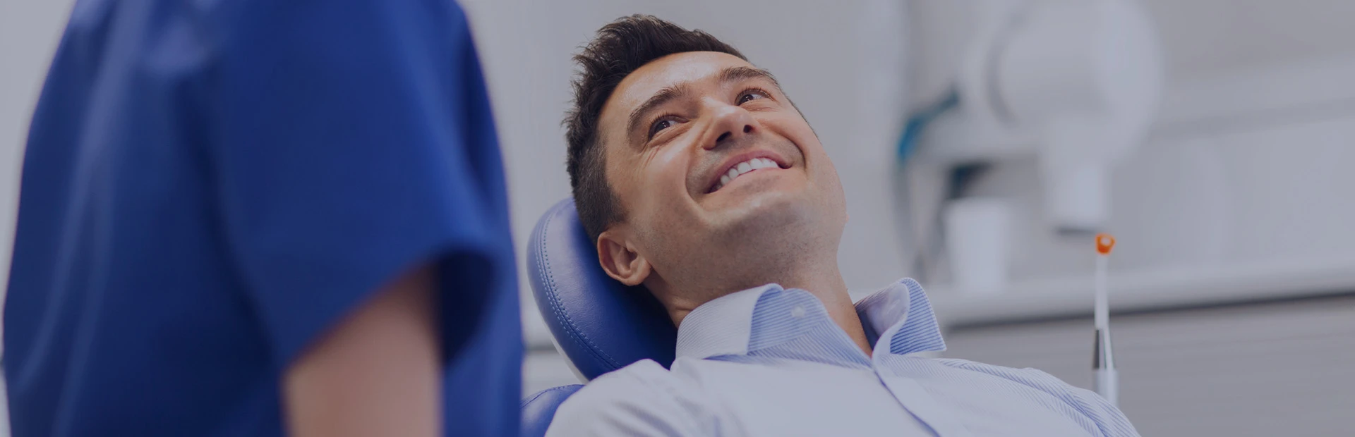 A man in his forties sits in the dentist's chair, as the dentist explains to him how to get rid of denture sores.