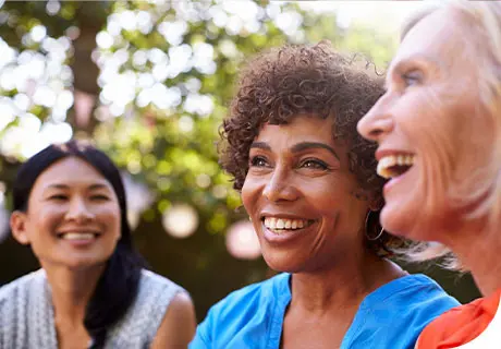 A group of female friends aged fifty and are outside in a park, smiling and laughing as they discuss how much do dental implants cost. 