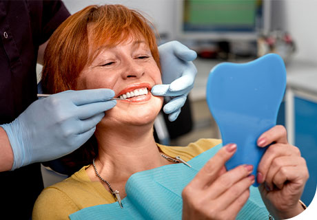 A woman in her 60s is in the dentist's chair smiling, because she knows the correct cleaning and maintenance procedure for her dentures, thanks to Fixodent. 