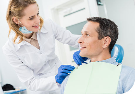 A dentist explains the denture-related dental procedures to a smiling male patient, who sits in a dental chair. 