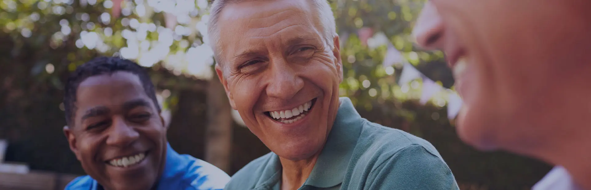 A group of male friends in their fifties are smiling in a garden, as they discuss getting used to full or partial dentures.