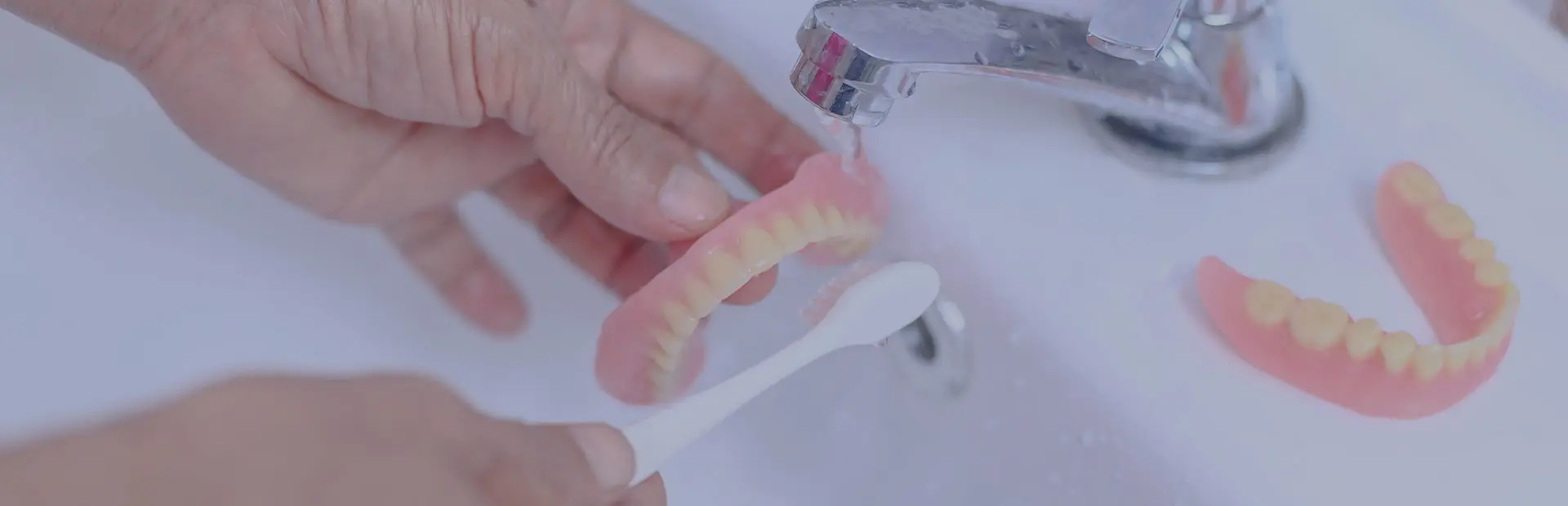 A close up of a soft toothbrush and dentures, as it's important to remove dentures to brush them for correct denture care and cleaning and remove them for repair, even when using Fixodent. 