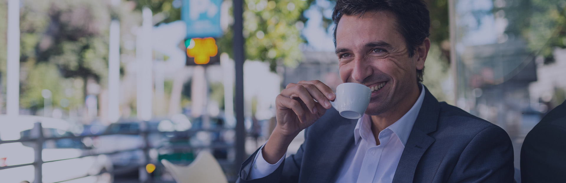 A man in his 40s sips an espresso on an outdoor terrace with a smile, as he knows how to remove stains from dentures thanks to Fixodent. 