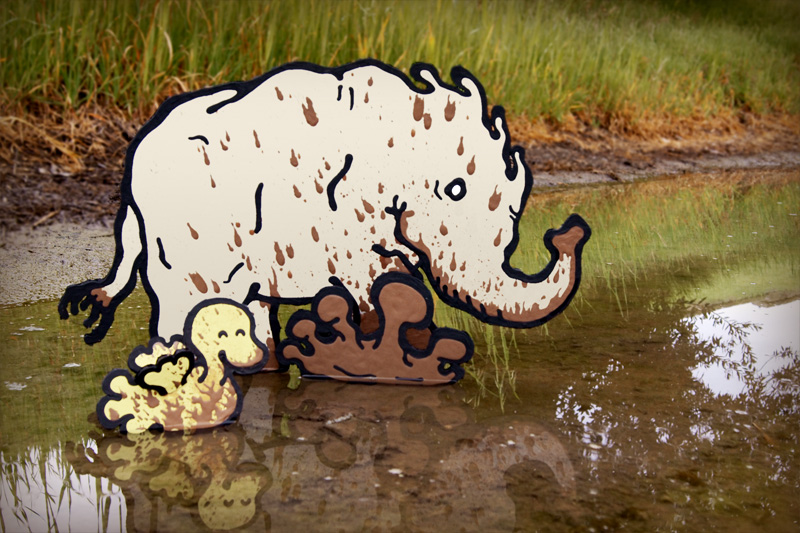 Cardboard elephant and cardboard bird enjoying splashing in the mud