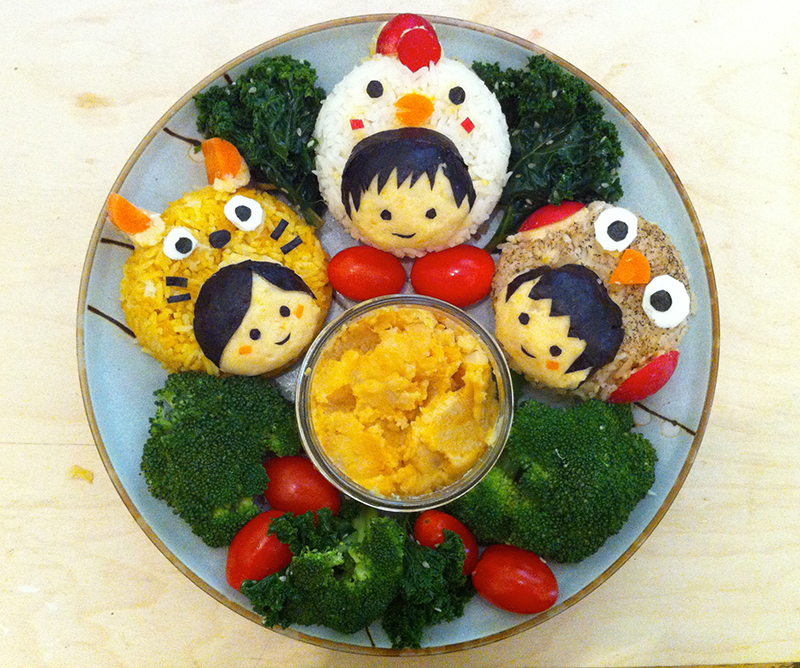 Three kid faces in a cat, chicken, and owl costumes made of different colors of seasoned rice plus nori decorations.