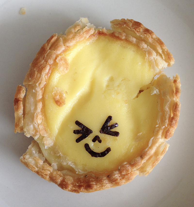 Dim sum egg tart decorated with a face made of nori.