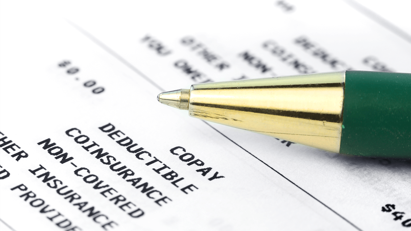 zoomed in view of ballpoint pen laying on top of insurance paperwork that says "copay, deductible, coinsurance, non-covered"
