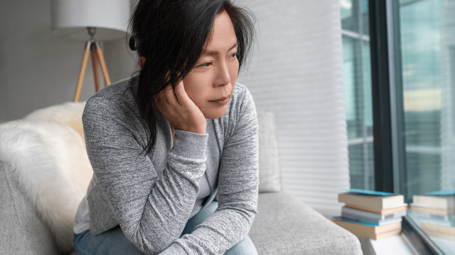 middle aged asian women with depression looking out window with sad expression