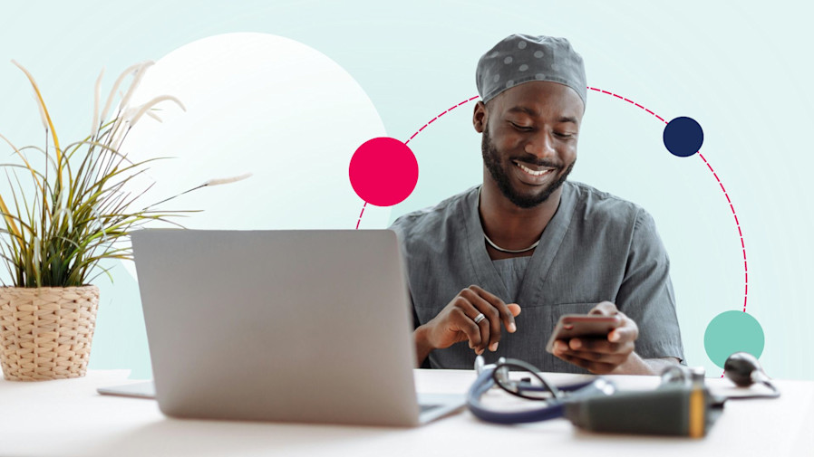 male nurse sitting at a desk on his laptop and smiling