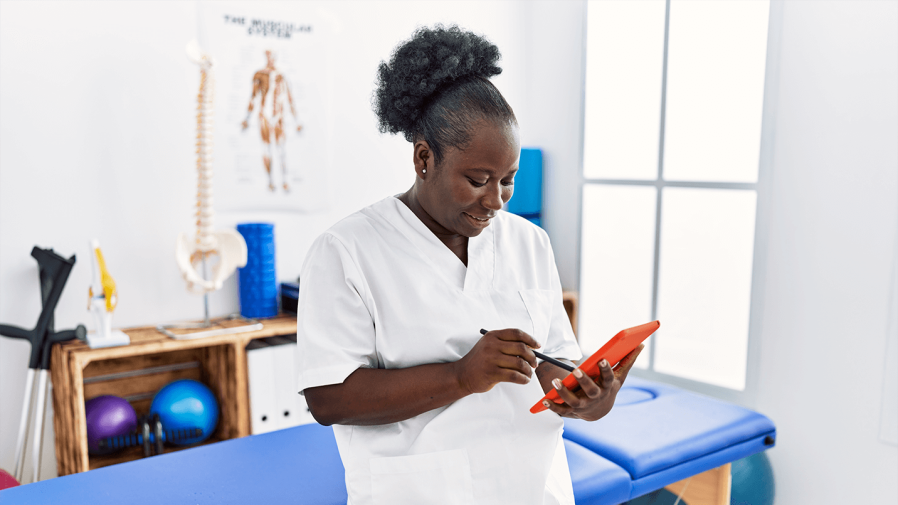 middle aged black female physical therapists looks a patient data on tablet