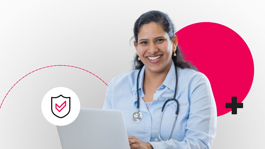 female doctor smiling at the camera and sitting at a desk with a laptop