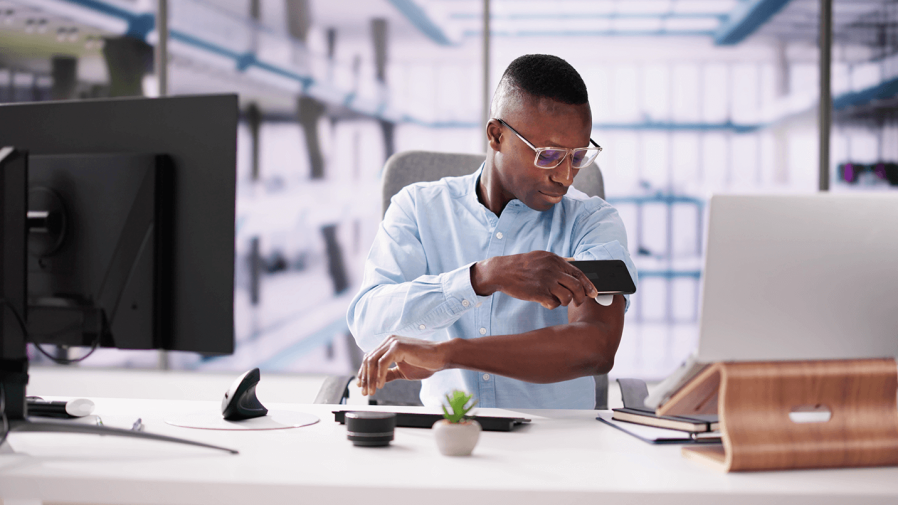 black man sitting at office desk and checking his A1c with a continuous glucose monitor