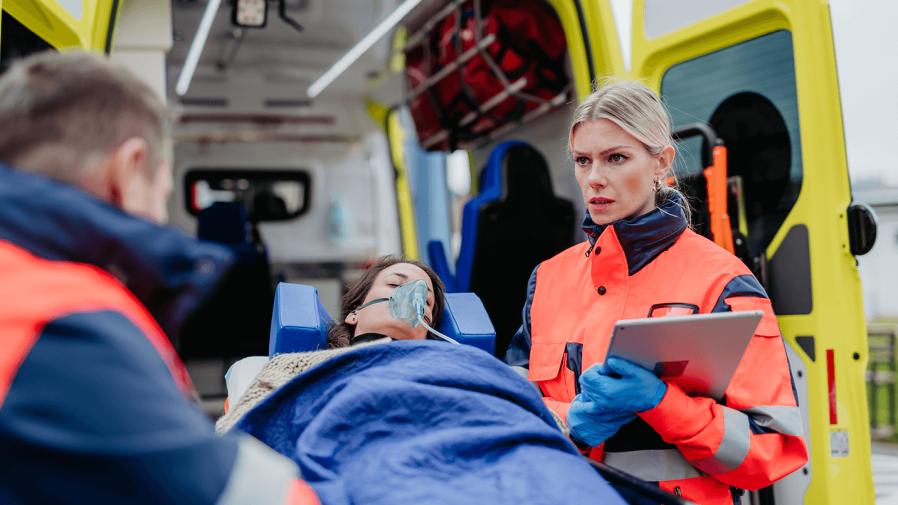female and male emergency medical responder loading patient into ambulance while female provider inputs patient data into her iPad 