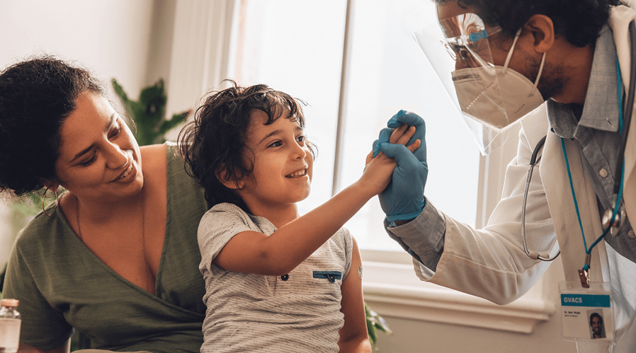 Child-sitting-on-mother's-lap-while-holding-healthcare-provider's-hand