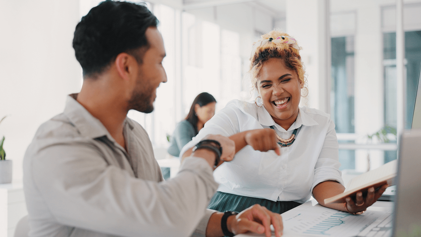 two co-workers laughing and fist bumping while working on a project