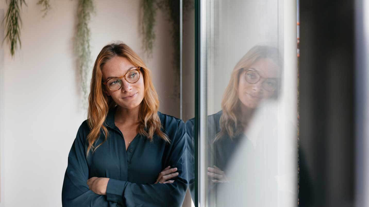 women leaning against a wall with her arms cross and looking out the window